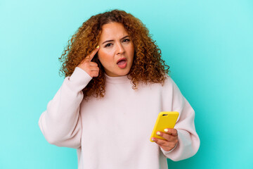 Young latin woman holding mobile phone isolated on blue background showing a disappointment gesture with forefinger.