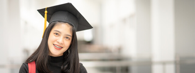 Young happy Asian woman university graduate in graduation gown and cap in the college campus....