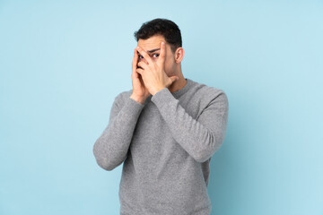 Young caucasian handsome man isolated on blue background covering eyes and looking through fingers