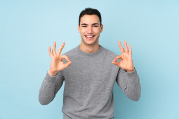 Fototapeta premium Young caucasian handsome man isolated on blue background showing an ok sign with fingers
