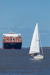 A sailboat in front of a huge container ship on Elbe river