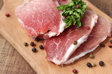 Raw pork chops on cutting board. Uncooked meat steaks for grilling with spices, pepper, salt and greens on wooden background. Top view 
