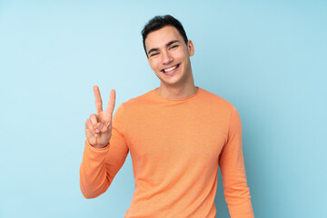 Young caucasian handsome man isolated on blue background smiling and showing victory sign
