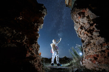 Back view of spaceman in white suit and helmet standing and exploring beautiful starry sky at night. Concept of cosmic traveler. © anatoliy_gleb