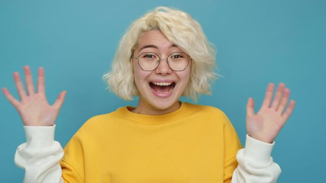 Portrait asian young woman face close up fearfully screaming raises hands her curly hair in glasses on blue background emotions. Freedom. Lifestyle Concept of emotions