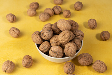Pile of walnuts inside a bowl on a yellow background