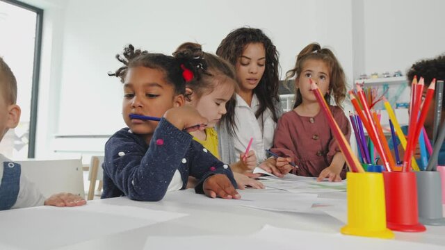 Kids drawing together in the kindergarden with a teacher.