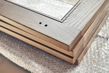 New smooth wooden frames for furniture facades lie on plastic protective covering in carpentry workshop extreme close view