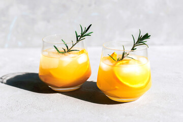 Cocktails with fresh orange wedges and a rosemary sprig under the bright rays of the sun. Summer refreshments.