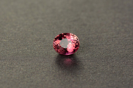 Natural unheated pinkish red color oval faceted transparent loose tourmaline gemstone setting from Mozambique for making jewelry. Isolated on gray pattern semireflective sparkling background.