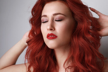 Fototapeta premium Close-up of beautiful young woman with red hair posing over grey background. 