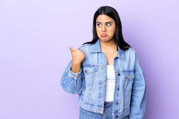 Young latin woman woman over isolated background unhappy and pointing to the side