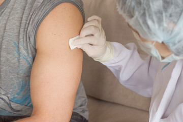 A nurse treats the injection point on the man's arm with an alcohol napkin.