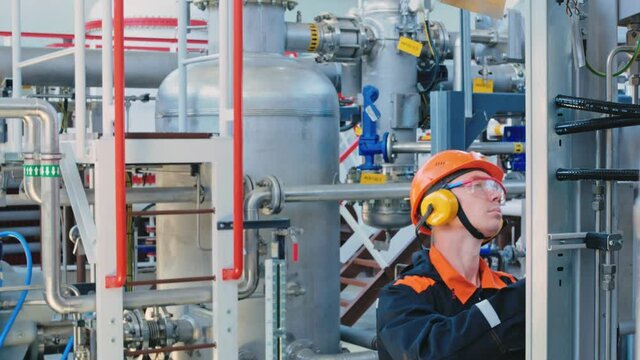 An engineer technician in a helmet, goggles and headphones, writes down the data on the operation of the equipment with a pen on a sheet of paper. Work in industrial. Manufacturing industry.