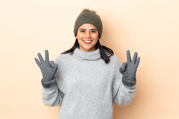 Young Colombian girl with winter hat isolated on beige background showing an ok sign with fingers