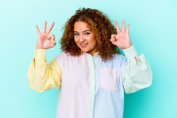 Young latin curvy woman isolated on blue background cheerful and confident showing ok gesture.