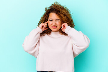 Young latin curvy woman isolated on blue background covering ears with fingers, stressed and...