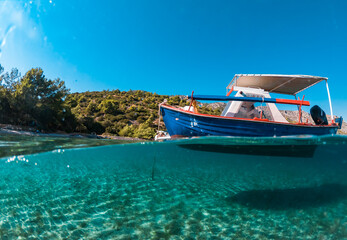 Half underwater photo of a boat in a beautiful beach of Samos island - obrazy, fototapety, plakaty