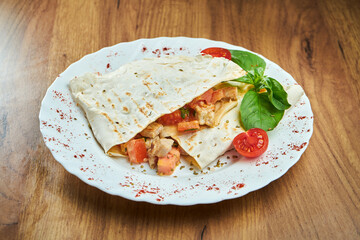An appetizing Mexican dish - quesadilla with chicken and tomatoes in a white plate on a wooden background.