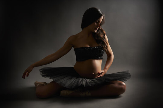 Portrait of a Hispanic pregnant ballerina performing classical ballet pose with blacktop and tutu