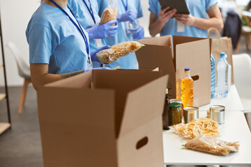 Cropped shot of volunteers in protective gloves sorting, packing food in cardboard boxes, working...