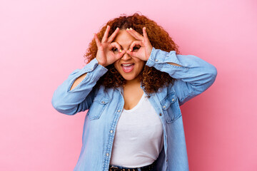 Young latin curvy woman isolated on pink background showing okay sign over eyes