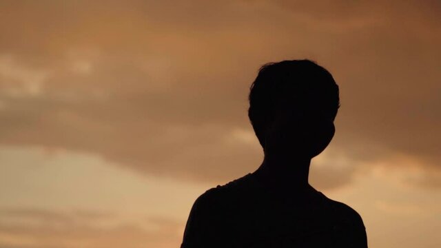 Silhouette of an Indian kid looking at the orange clouds during the sunset. 