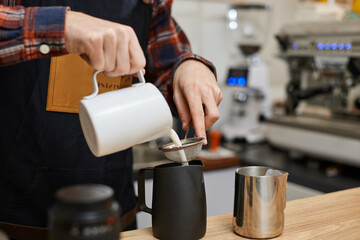 Caucasian man pouring hot milk in coffee.