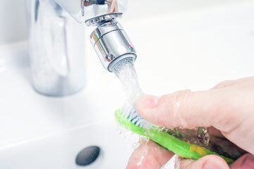 Cleaning A Toothbrush Under Pouring Water At Bathroom Sink