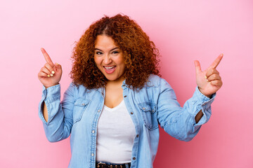 Young latin curvy woman isolated on pink background pointing to different copy spaces, choosing one of them, showing with finger.