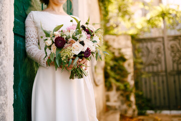 Bride holds in her hands a beautiful bouquet of flowers leaning against the green door of the building