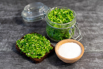 Wild leek pesto on a slice of bread with olive oil and salt on a wooden table with bread. Useful properties of wild garlic. Fresh bear onion leaves.