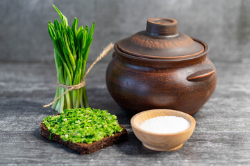 Wild leek pesto on a slice of bread with olive oil and salt on a wooden table with bread. Useful properties of wild garlic. Fresh bear onion leaves.