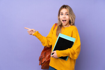 Teenager Russian student girl isolated on purple background surprised and pointing finger to the side