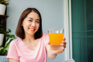 Mid-age Asian woman reading a book and hold orange juice glass in the home. Concept of  Health care And eating for healthy