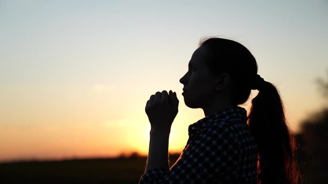Christian woman praying at sunset close-up. Girl on the background of the sky in the rays of the sun prayer to the family and children. Relaxation and meditation in nature, healthy lifestyle