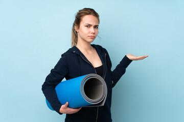 Teenager Russian girl holding mat isolated on blue background unhappy for not understand something