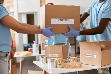 Cropped shot of diverse male volunteers in blue uniform, protective mask and gloves carrying...