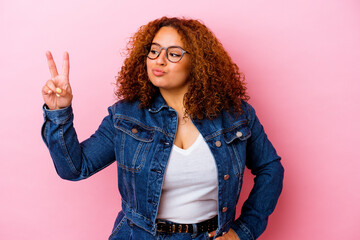 Young latin curvy woman isolated on pink background joyful and carefree showing a peace symbol with...