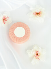 Round solid soap bar in pink paper package on white silk background