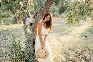 Tender portrait of beautiful brunette woman in beautiful sunlight. Woman in yellow summer linen dress in olive tree garden. Natural beauty.Travel to Italy, summer vacation - Powered by Adobe