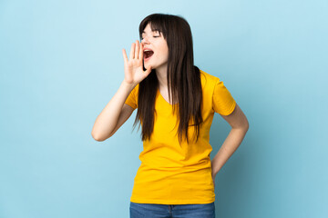 Teenager Ukrainian girl isolated on blue background shouting with mouth wide open to the side