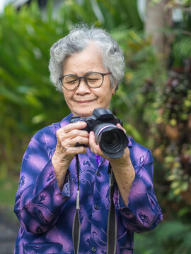 Happy senior woman viewing her photos in a digital camera while standing in a garden. Aged people photographer and relaxation concept