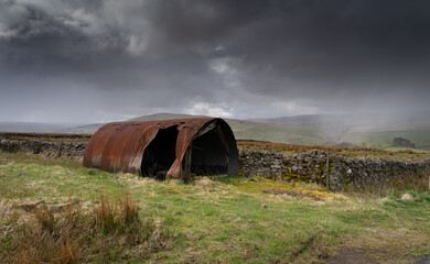 Fototapeta na wymiar old tin shed in the North Pennine landscape near Garrigill, Cumbria with a snow shower in the landscape behind