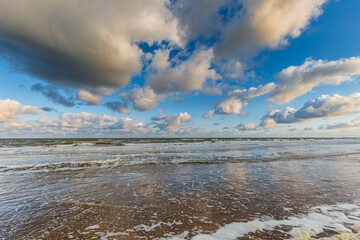 Seascape North Sea coast during sunrise and high tide with blue sky with scattered cumulus clouds...
