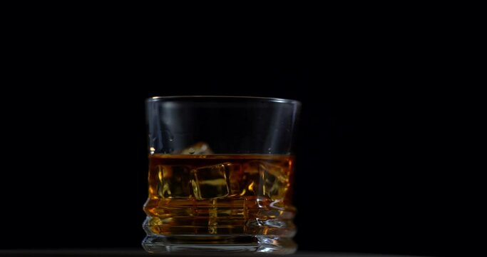 Whisky is in glass. Rotating with black background. Alcohol. Ice cubes in the glass. 4k. Scotch on the rocks. Slider shot. Dark, rustic