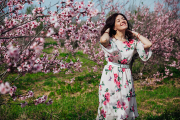 Beautiful brunette woman in a dress with flowers walks through the flowering garden in spring