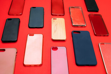 Pile of multicolored plastic back covers for mobile phone. Choice of smart phone protector accessories on red background. A lot of silicone phone backs or skins next to each other