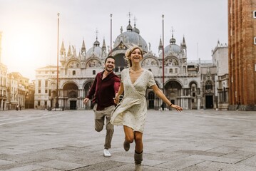 Fototapeta Couple of tourists visiting Venice, Italy - Boyfriend and girlfriend in love running together on city street at sunset - People, love and holidays concept obraz