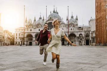 Fotobehang Couple of tourists visiting Venice, Italy - Boyfriend and girlfriend in love running together on city street at sunset - People, love and holidays concept © Davide Angelini